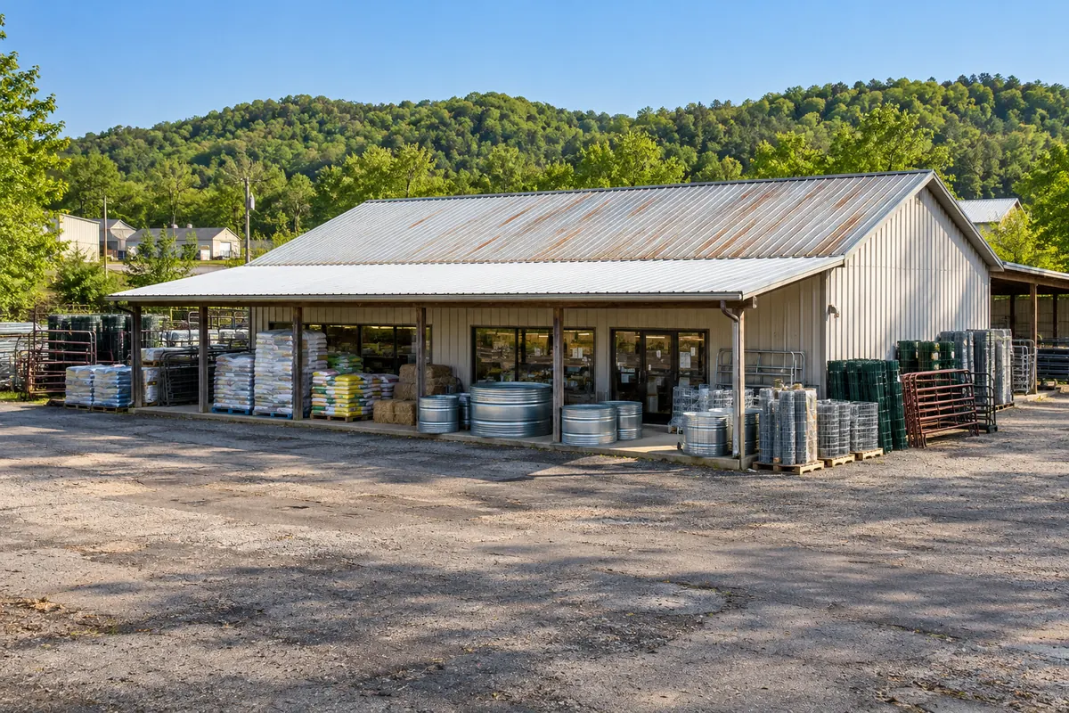 Open-front metal supply building with a long sloped roof and stacked materials